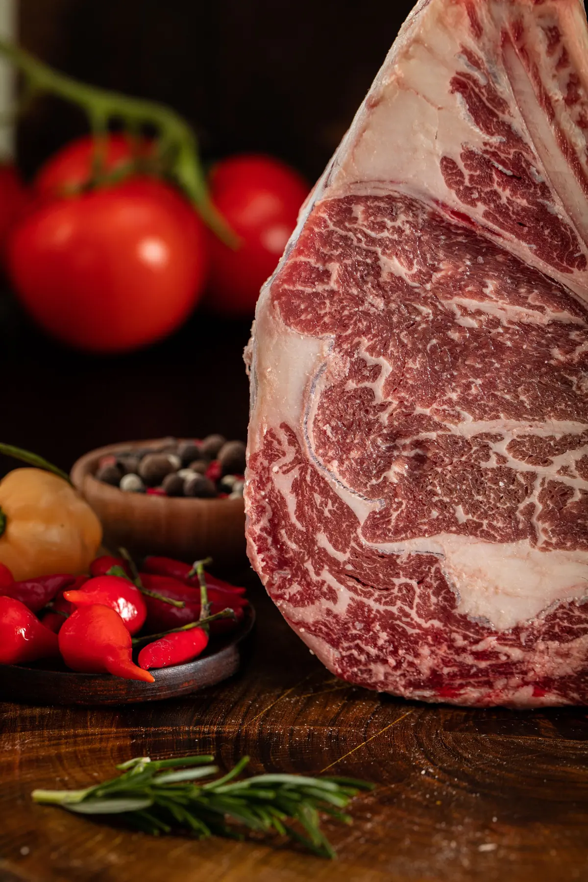 Rohes, marmoriertes Rinderstück am Knochen mit Pfeffer, Chili und Rosmarin auf rustikalem Holz