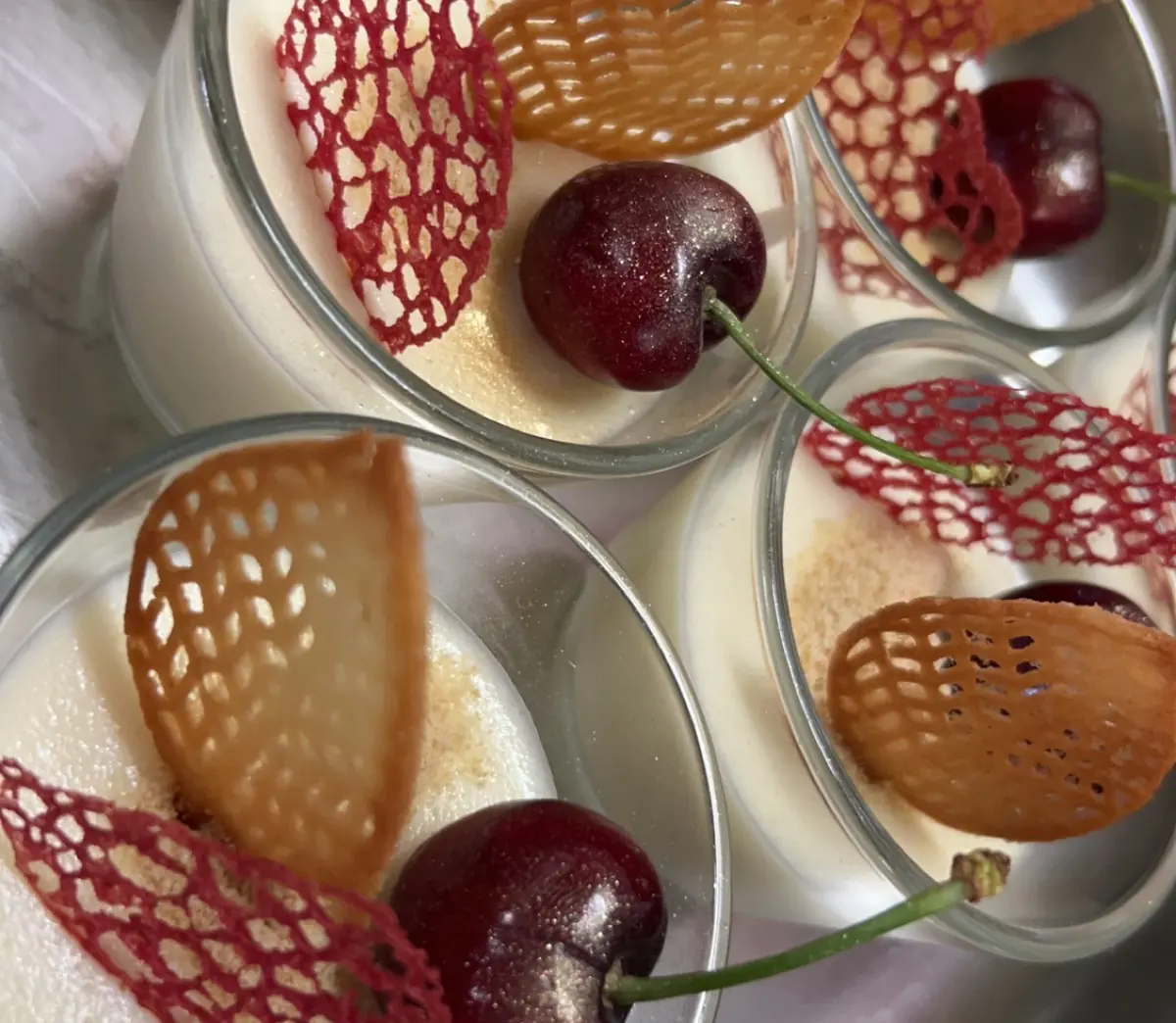 Panna cotta im Glas mit Kirsche und rotem und goldenem Zuckergitter